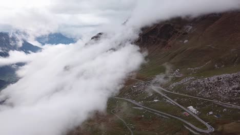 clouds moving over rocky mountain landscape criss-crossed by winding roads and snowy hills in the background