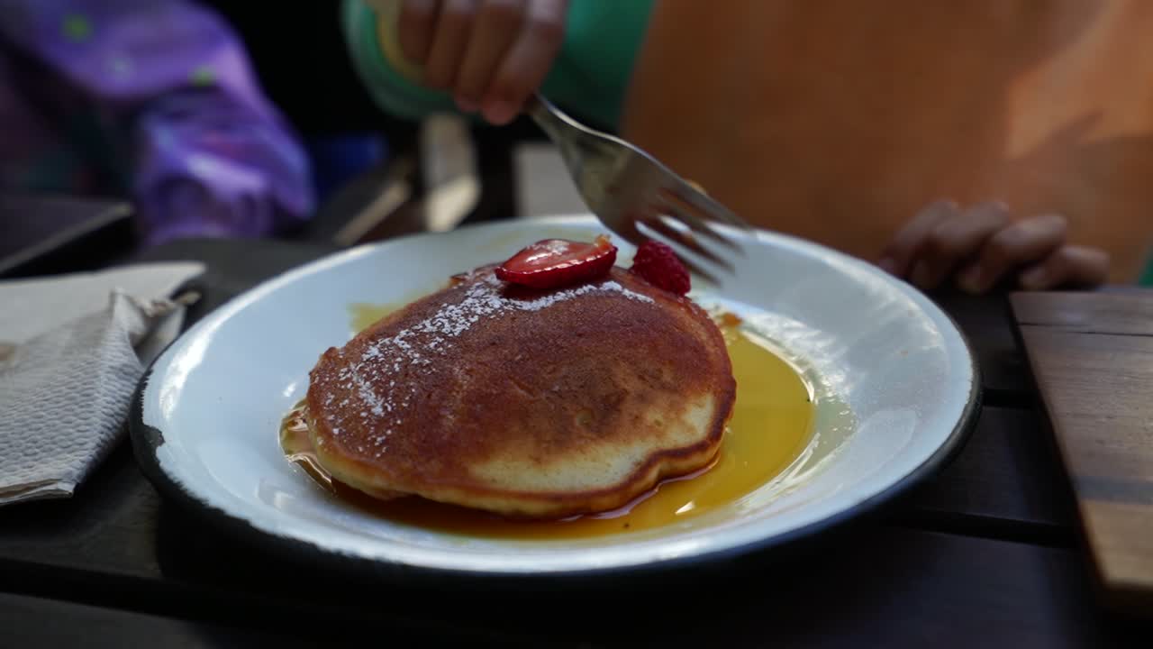 Kid eating breakfast, plate of medium size pancakes, honey and strawberry topping