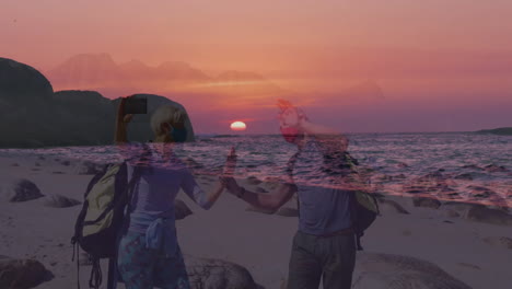 couple standing on rocky beach at sunset, holding smartphone and showing animated travel map pin