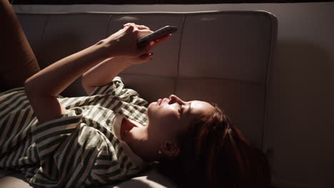 a woman relaxes a couch scrolling through her smartphone enjoying a tranquil afternoon.
