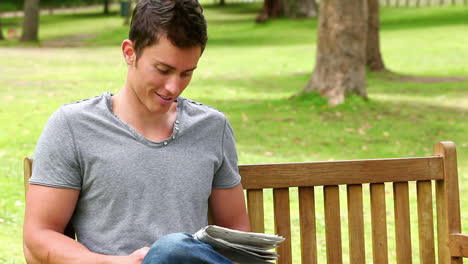 hombre leyendo un periódico antes de mirar a la cámara mientras se sienta en un banco