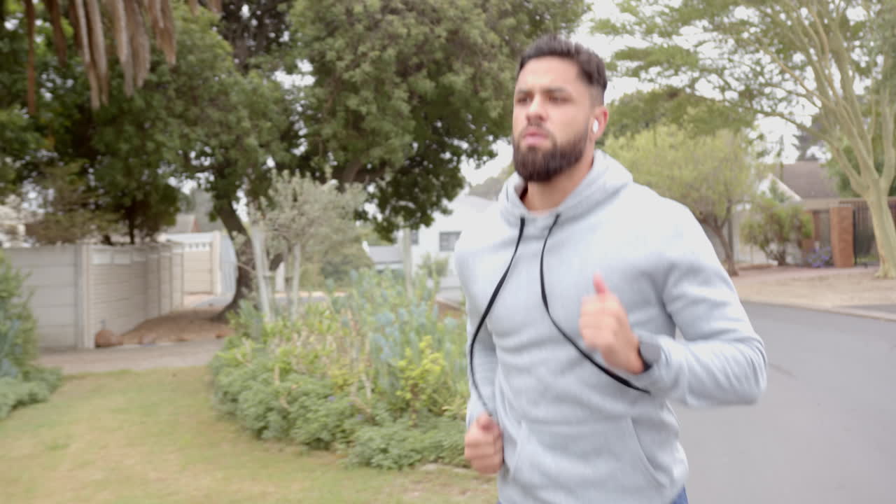 Running outdoors, man in hoodie exercising with wireless earbuds in residential area