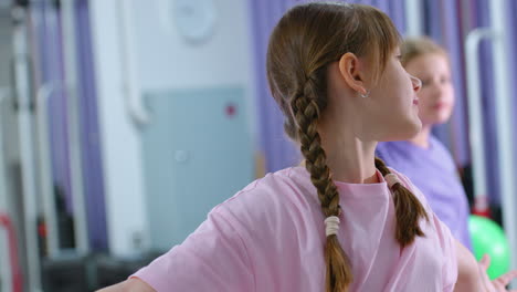 primer plano de chicas jóvenes en una sesión de entrenamiento sosteniendo globos mientras se estiran, expresiones enfocadas, entorno de gimnasio con equipos de fitness en el fondo