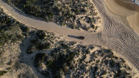 vehicle leaving beach and driving along unpaved road between sandy dunes, australia