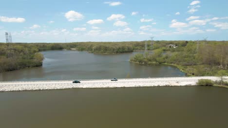 aerial horizontal pan of moving vehicle, suv, on a rural road near a lake in the suburbs