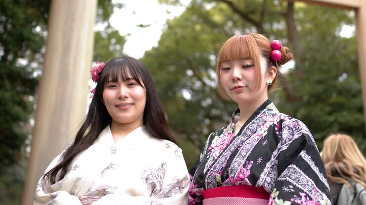 Inquadratura dal basso di due amici in kimono floreali che sorridono davanti a un torii.