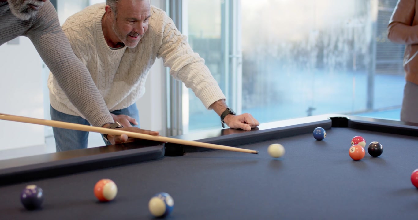 Diverse male friends leaning over black felt pool table with cue, one pointing, aiming for pocket