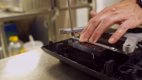 Close up shot on man's hands assembling a professional kitchen weight scale, screw bolt on battery holder, 4k