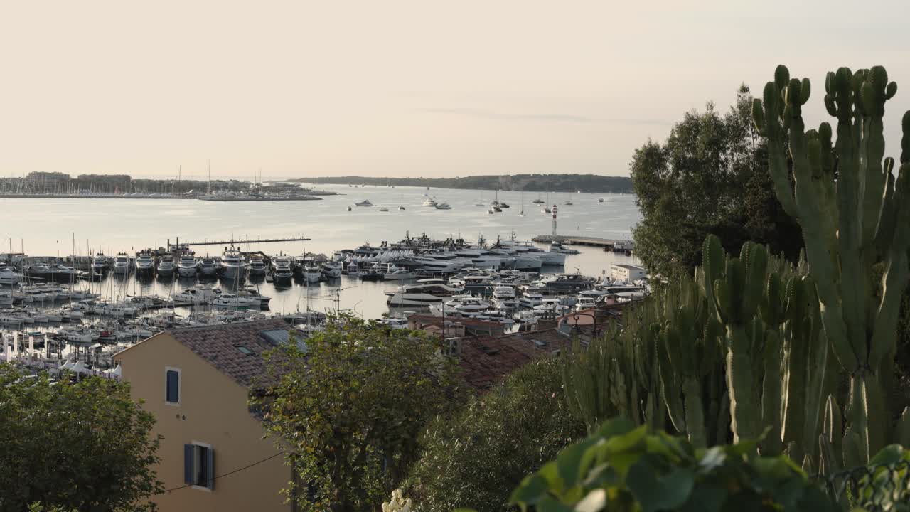 Clip video girata da una posizione elevata a Cannes, in Francia, che mostra una vista panoramica verso il porto e l'area urbana circostante. Acquisita al mattino presto durante l'alba, con una luce calda
