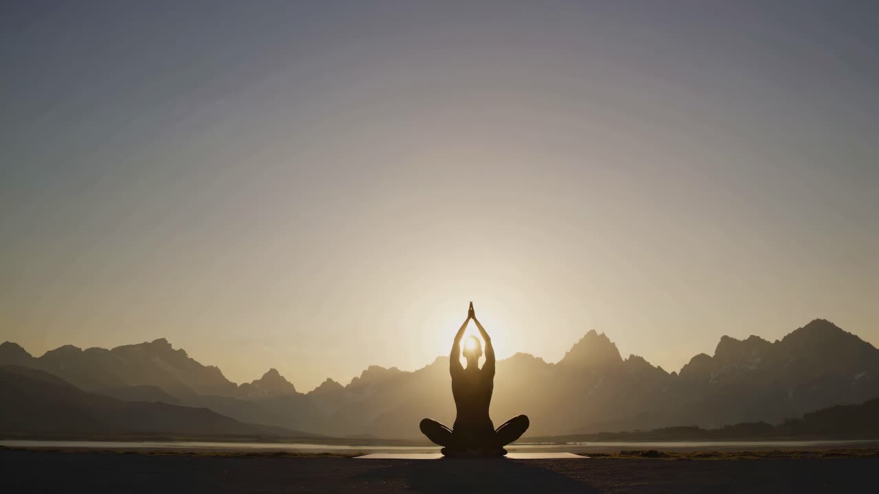 Silhouette di una persona che medita all'alba, con montagne sullo sfondo