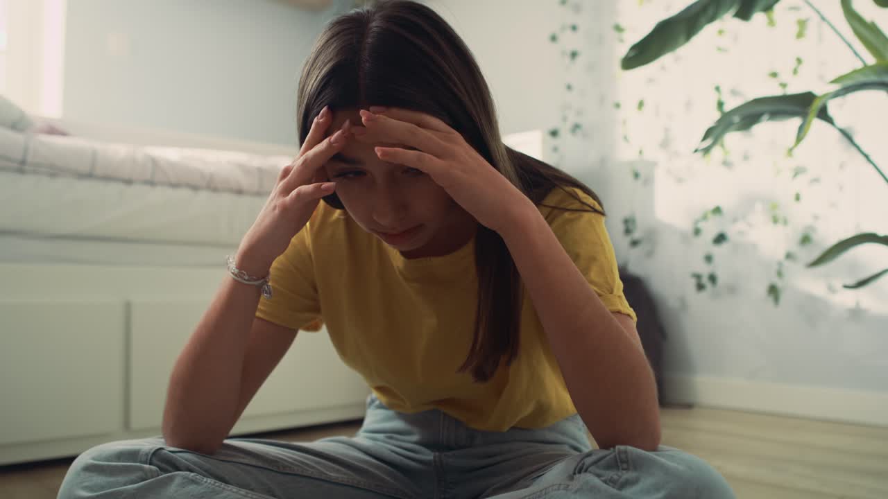 손에 머리를 들고 바닥에 앉아서 배우려고 하는 백인 십대 소녀를 확대