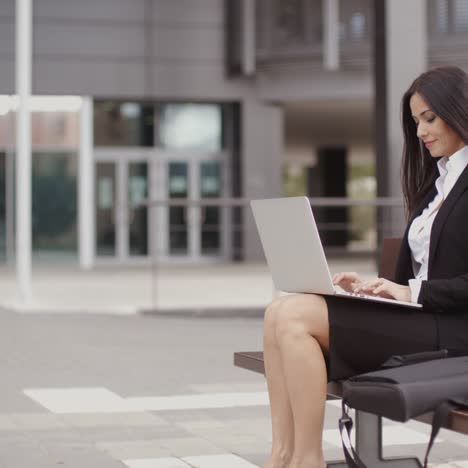 Woman-sitting-with-laptop-on-bench-outdoors