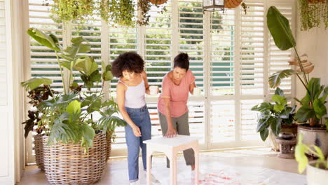 assembling furniture, mother and adult daughter working together in bright living room with plants