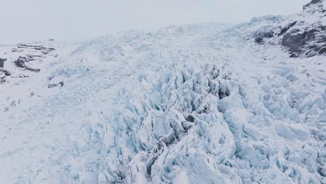 Aerial-landscape-view-over-ice-formations-in-Falljokull-glacier-covered-in-snow,-Iceland,-at-sunset