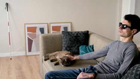 Side-View-Of-A-Blind-Man-In-Sunglasses-Sitting-On-The-Sofa-At-Home-And-Petting-His-Cat-2