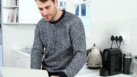 hombre usando una computadora portátil mientras toma café en la cocina