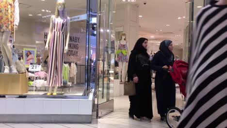 people walking through a shopping mall with store windows and mannequins