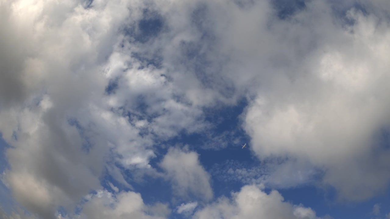 Wide view of an airplane flying across a blue sky with clouds