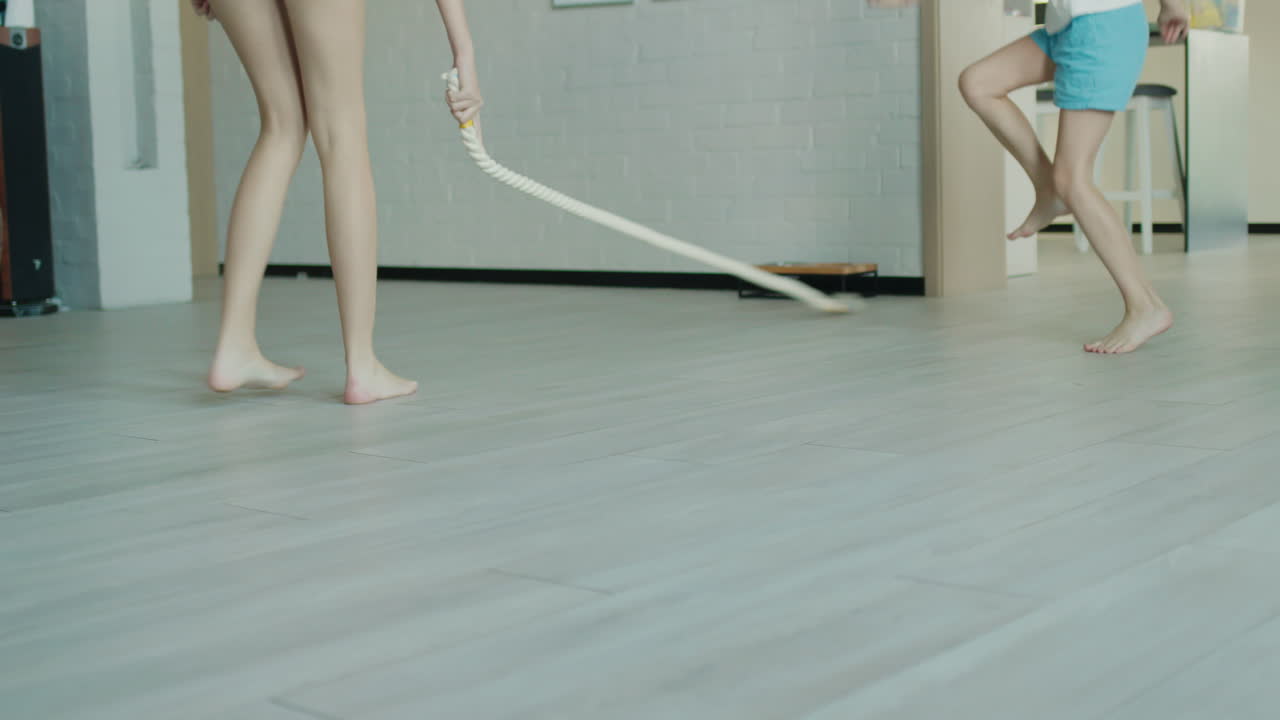 아이들은 거실에서 강아지와 함께 놀고 있습니다. 다리와 강아지만이 프레임에서 보이는데, 그것은 로프를 잡으려고합니다.