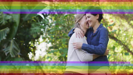 animation of pride rainbow stripes over happy caucasian lesbian couple embracing in garden