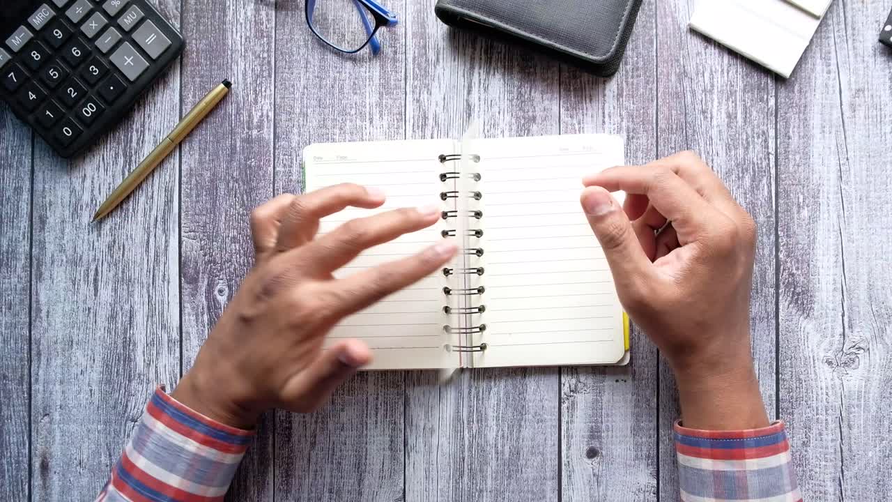 Person holding an open notebook on a wooden desk