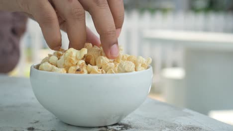 person's hand reaching for popcorn in a white bowl