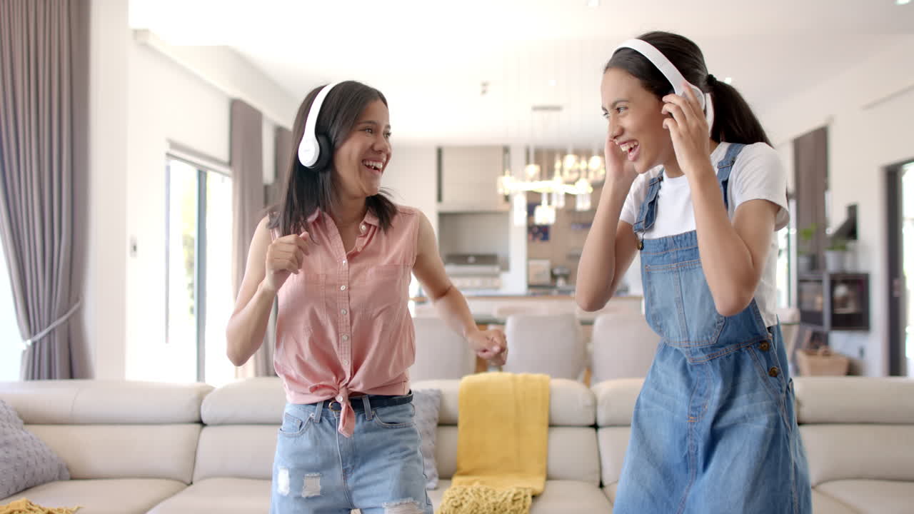 Listening to music with headphones, two teenage girls laughing and dancing