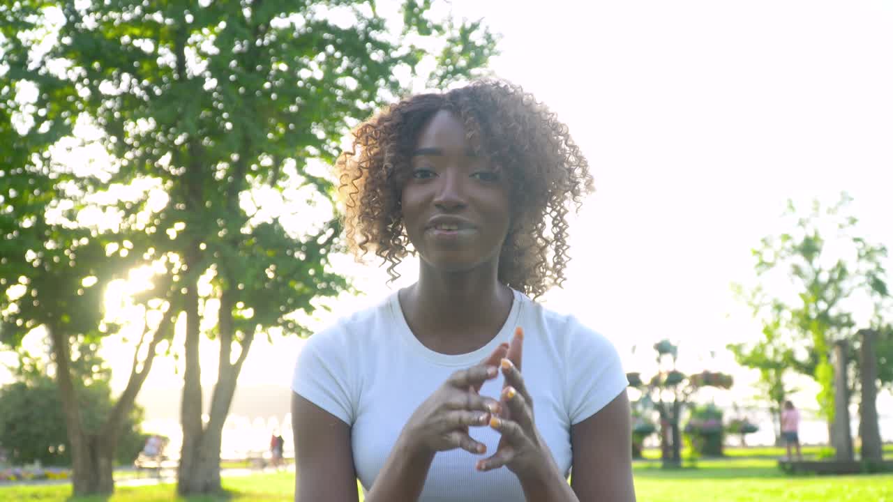 Smiling young african woman blogger influencer sit in park speaking looking at camera talking make video conference call record lifestyle blog concept, webcam view