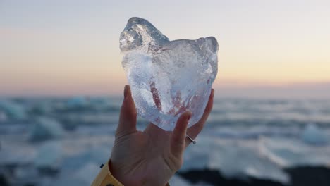 mujer sosteniendo un gran bloque de hielo en la playa de diamantes en islandia