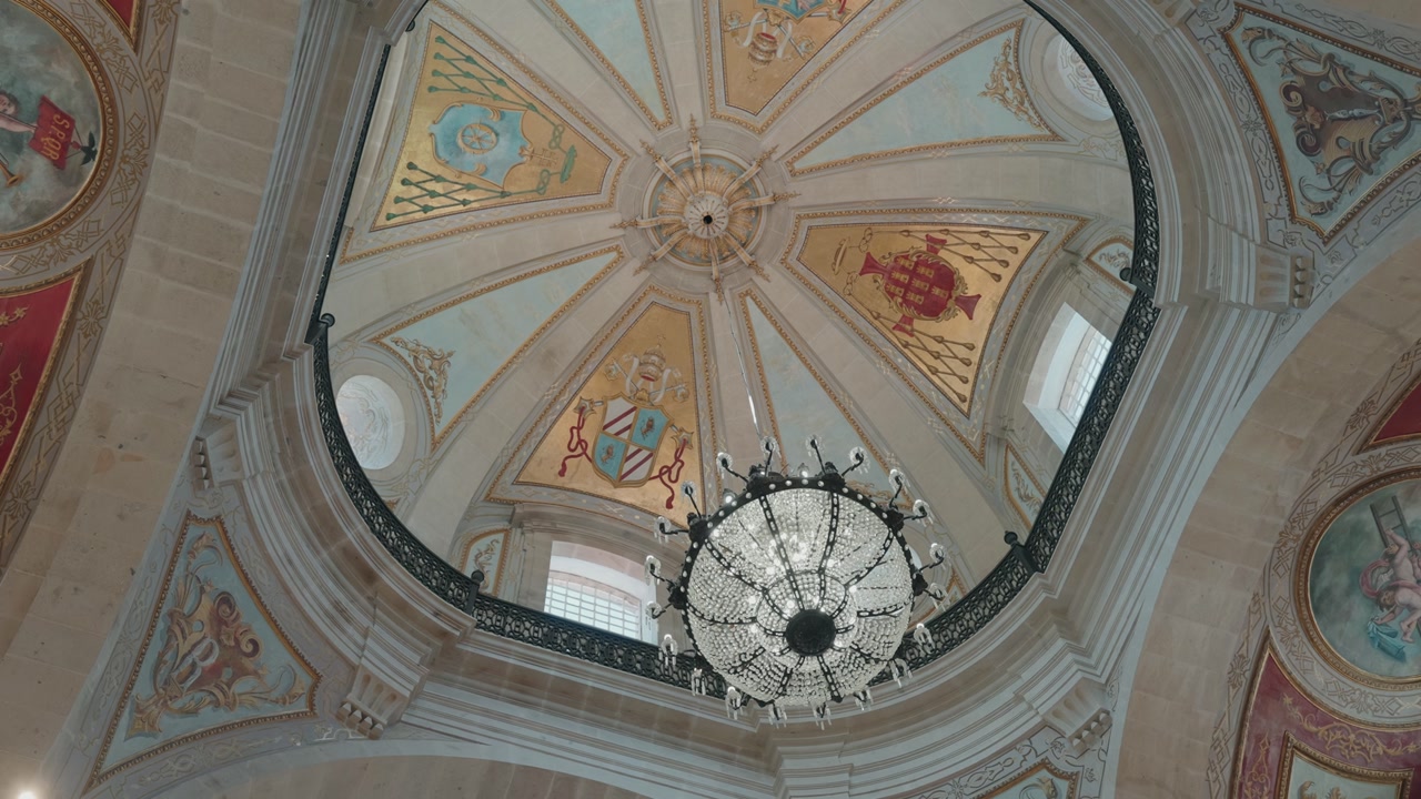 Interior view of a church dome featuring a grand chandelier and colorful painted heraldic symbols