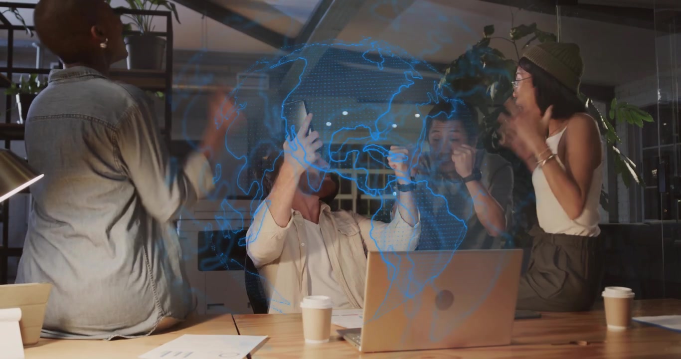 Tech team tapping smartphone and projecting holographic globe above laptop while celebrating win