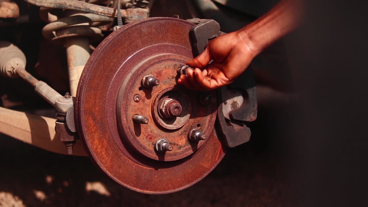 Close-up of mechanic’s hand tightening wheel nuts on rusty disc brake hub, using wrench.