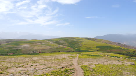 panoramic view of green and yellow agricultural fields on rolling hills with distant mountains under a cloudy sky