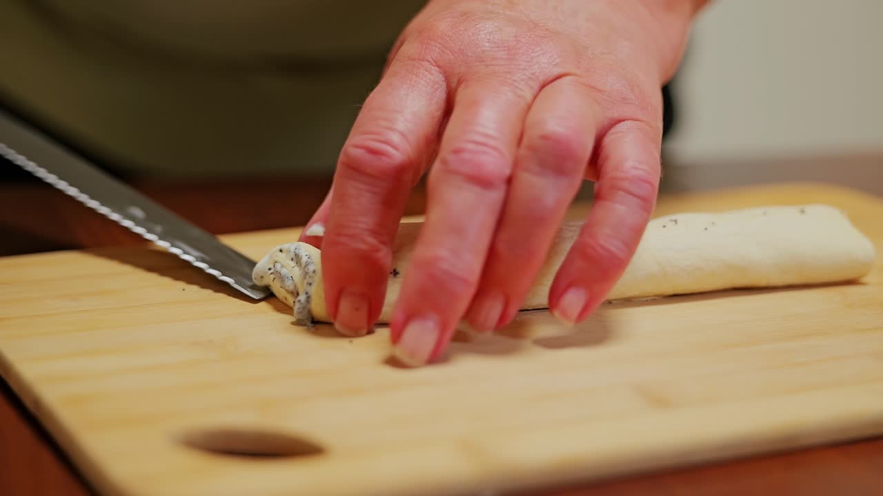 Slow motion shot of woman’s hands slicing poppy dough roll in warm kitchen