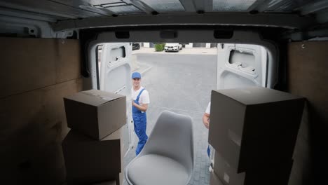 two young workers of removal company unload boxes and furniture from minibus into customer's home