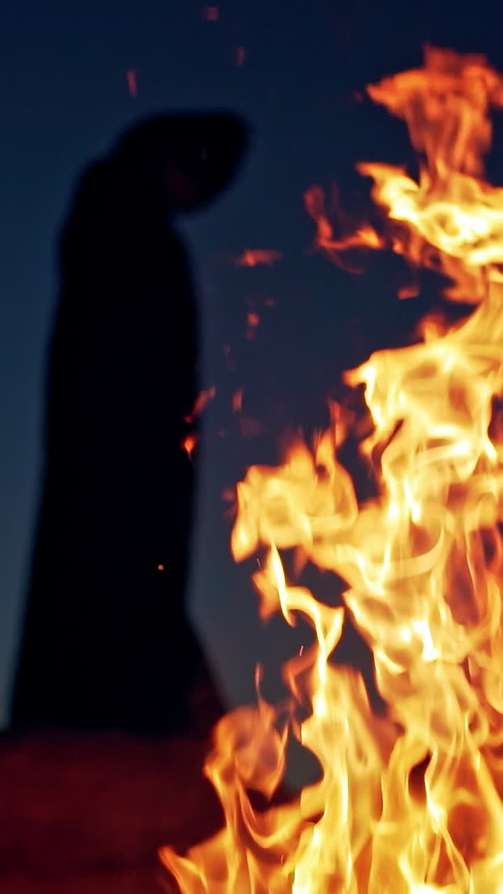 Witch on Halloween Day. Witch in cloak with hood near the fire in forest . Vertical video