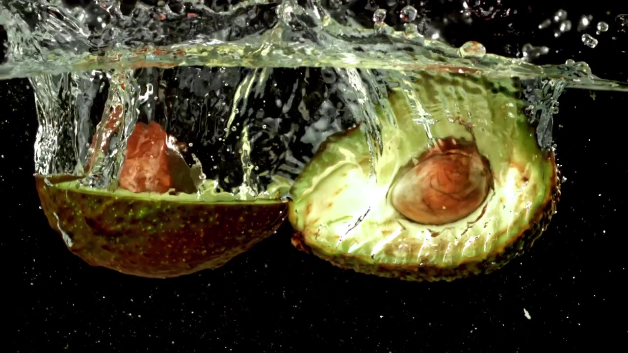 Mezzi avocado maturi che schizzano nell'acqua al rallentatore