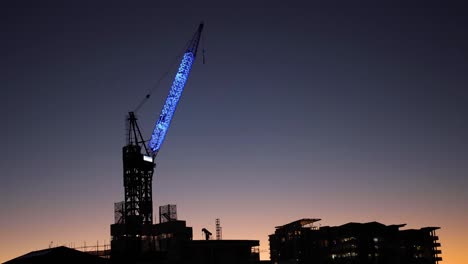 grúa iluminada que opera contra el cielo del crepúsculo