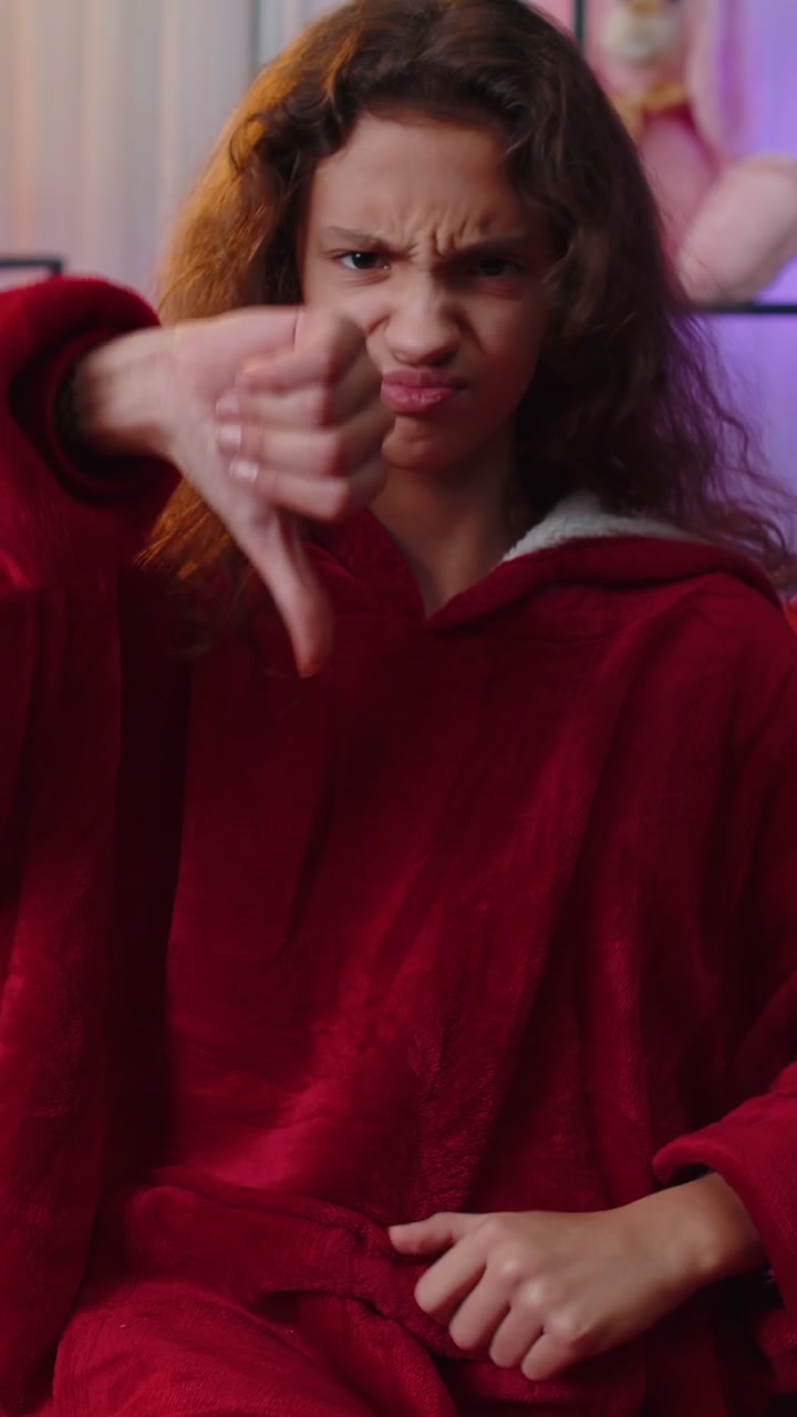 Upset young girl showing thumbs down dislike bad work disapproval dissatisfied feedback at home