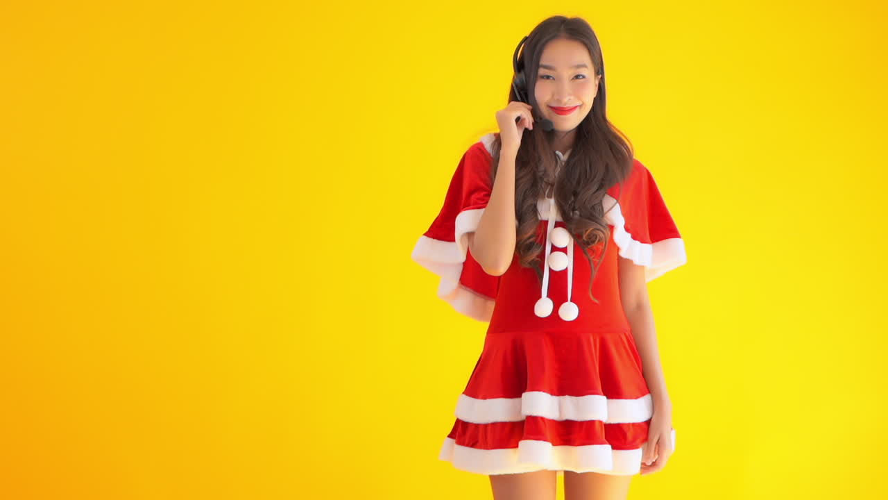 A young sassy woman dressed in a red Santa's helper suit wears a headset to answer calls from around the world. Copy space
