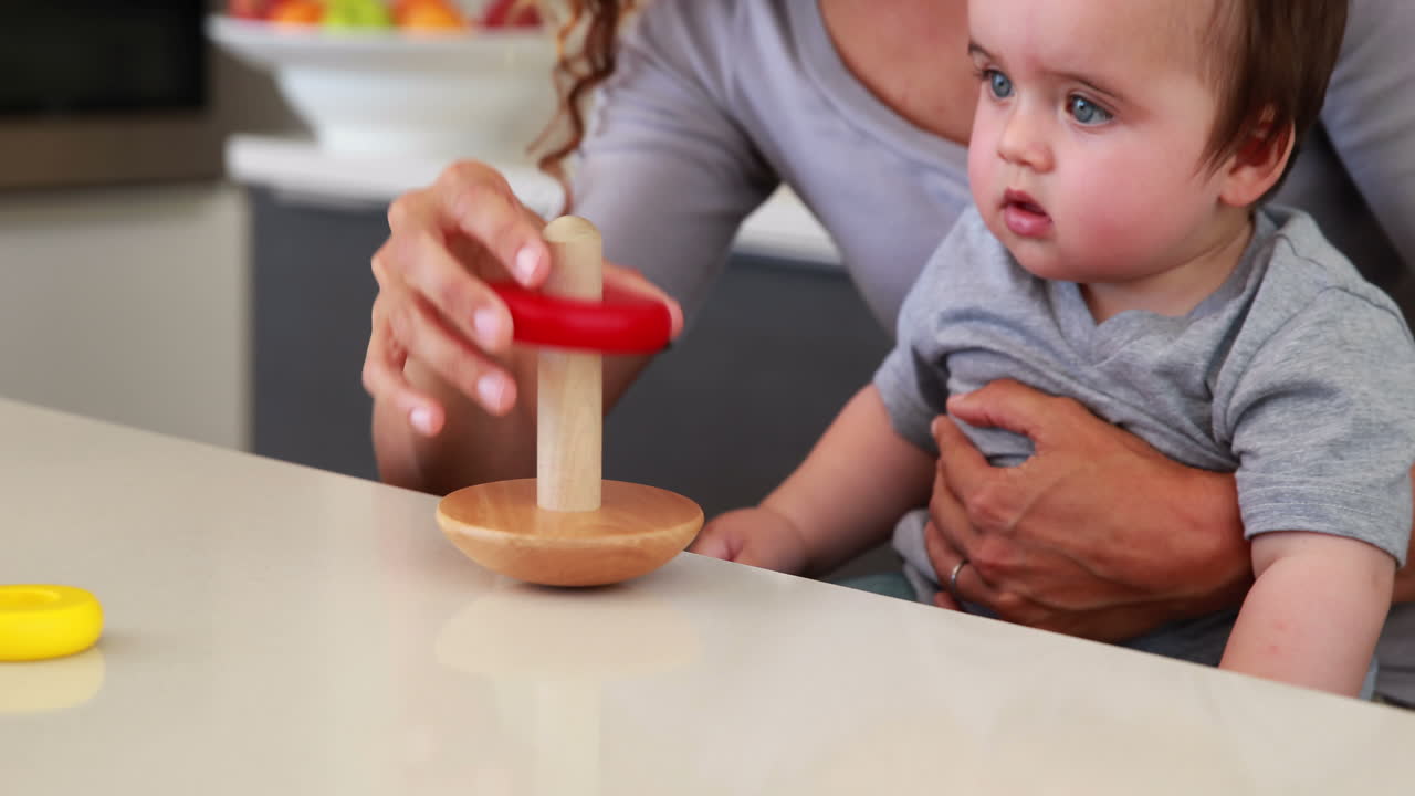 Mother sitting with baby boy on lap playing with wooden toy