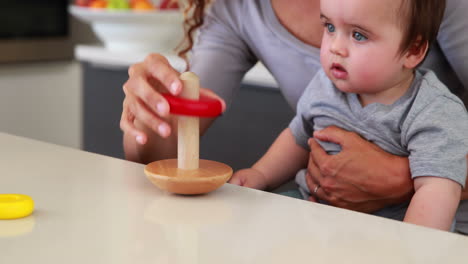 madre sentada con el bebé en el regazo jugando con un juguete de madera