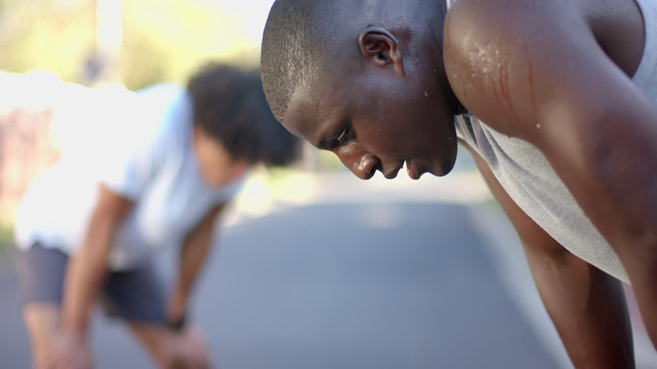 Exercising outdoors, two multiracial male friends resting and catching breath, running, copy space