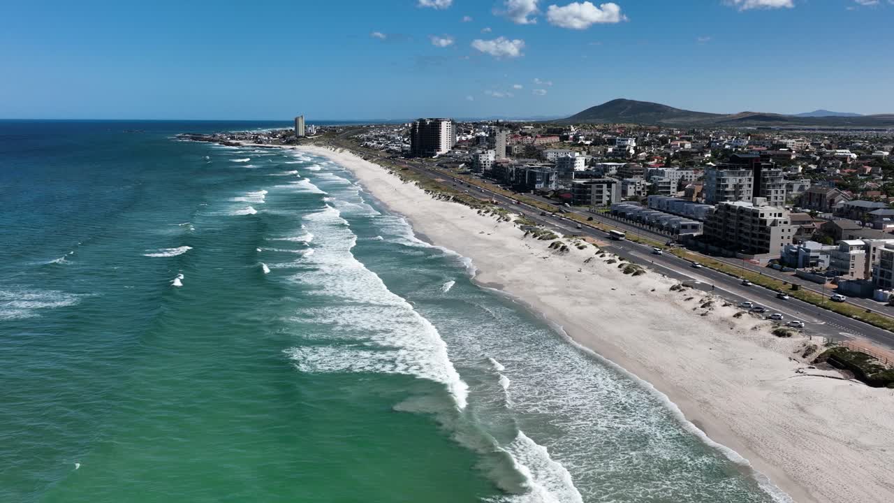 vuelo de drones sobre la costa de bloubergstrand con edificios frente al mar en ciudad del cabo, sudáfrica, en un día soleado