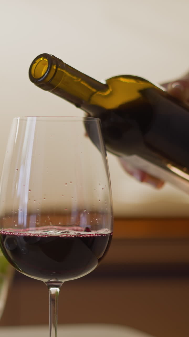 una mujer llena un elegante vaso de vino con vino tinto vintage envejecido de una botella que sirve una cena romántica festiva en casa.