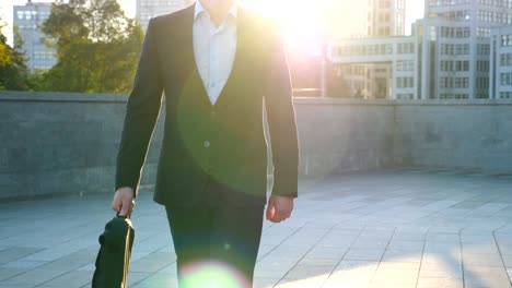 young businessman with a briefcase walking in city street. business man commuting to work in the urban environment. confident guy in suit being on his way to work. cityscape background. slow motion