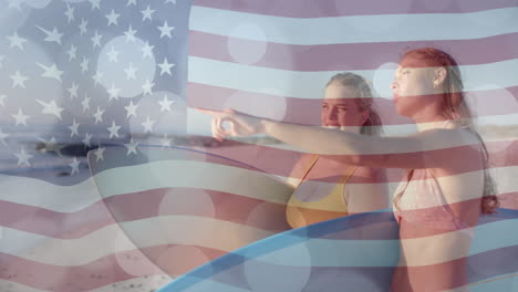 Animation-of-flag-of-usa-over-happy-caucasian-women-with-surfboards-on-beach-in-summer