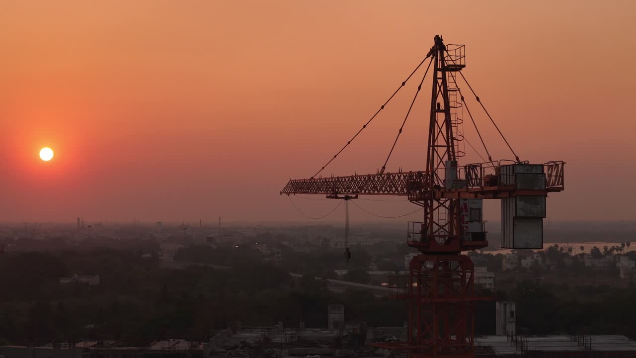Silhouette construction crane standing against vibrant sunset. Aerial view.