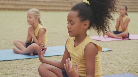 Video-of-focused-diverse-girls-practicing-yoga-on-mats-in-front-of-school