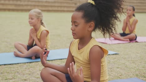 video de niñas diversas enfocadas practicando yoga en esteras frente a la escuela